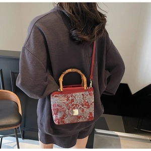 Detail of red embroidered bucket bag with natural bamboo handle and golden hardware