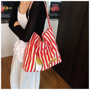 Vue latérale d'un grand sac cabas rayé avec broderies et écussons porté par un modèle