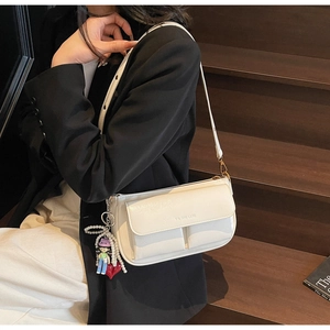 Detail of white glossy shoulder bag with pearl charm pendant on a model in black suit