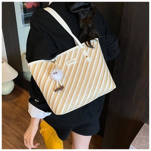Close-up of woven tote bag with yellow stripes and cute white plush charm accessory