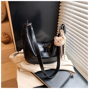 Detail of black crocodile texture hobo bag with teddy bear charm on minimalist background