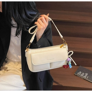 Detail of cream pillow bag with gold hardware and a pearl bow charm on dark steps
