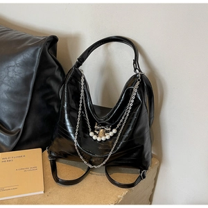 Nahaufnahme der glänzenden schwarzen PU-Tasche mit Silberkette, Perlen und Schleife