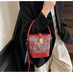 Close-up of a red bucket bag with traditional white cloud embroidery and gold metal clasp