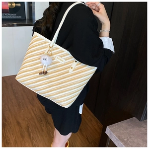 Détail du sac cabas en paille à rayures jaunes et blanches avec écusson en cuir et charm