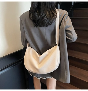 Chic cream-colored leather crescent bag worn over a grey blazer on wooden stairs