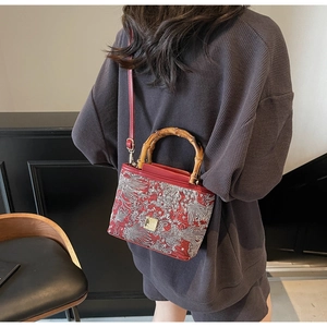 Detail of red embroidered bucket bag with natural bamboo handle and silver floral pattern