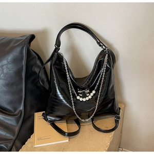 Detailaufnahme des glänzend schwarzen Rucksacks mit Perlenkette und Metallbogen