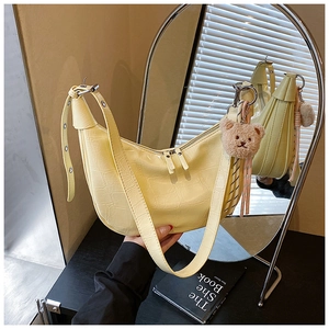 Detail of light yellow crocodile embossed crescent bag with cute brown teddy bear charm