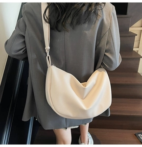 Close-up of off-white lychee grain leather crescent bag worn by a model on stairs