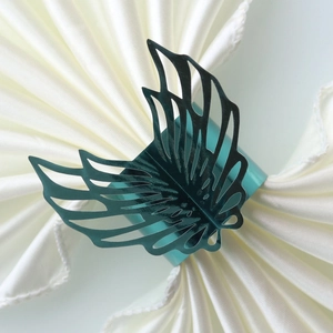 Detailed laser-cut turquoise butterfly napkin ring with metallic shimmer on white satin