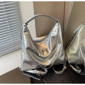 Detailansicht der silbernen Hobo-Tasche mit Metallic-Struktur, Perlenkette und Goldbogen