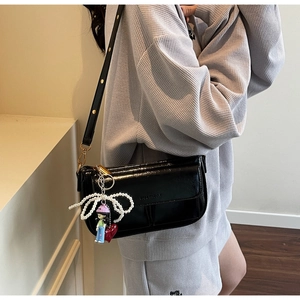 Detail of black glossy leather crossbody bag with pearl bow and cartoon girl pendant