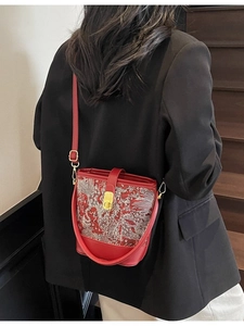 Red crossbody bag with silver embroidery on black suit model against wooden stairs