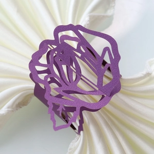 Detailed view of purple laser-cut rose napkin ring on a white satin cloth for weddings
