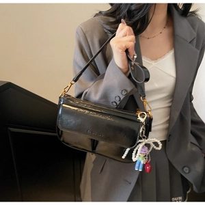 Detail of black patent leather shoulder bag with gold hardware and pearl bow charm