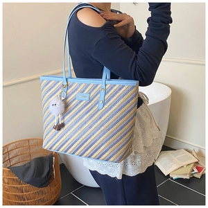 Detail of woven tote bag featuring blue and yellow stripes and a soft plush pendant