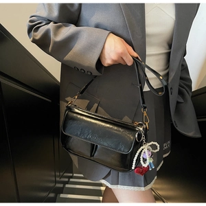 Glossy black underarm bag with gold zippers and pearl heart charm shown on model