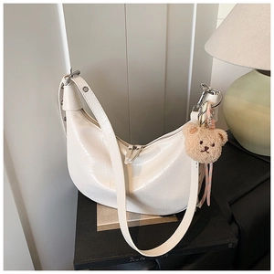 Detail of white crocodile embossed dumpling bag with double zippers and plush bear charm