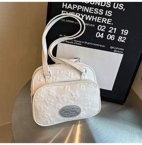 Détail du sac à main blanc texturé floral avec plaque argentée sur table industrielle