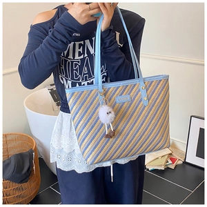 Détail d'un sac cabas tissé avec rayures diagonales bleu et jaune et charm en peluche blanc