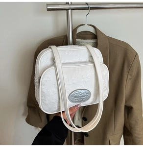 Détail d'un sac à main blanc avec gaufrage floral et plaque logo décorative en métal