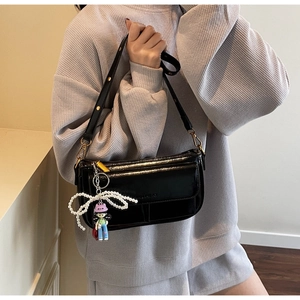Detail of glossy black patent leather shoulder bag with pearl bow and girl charm