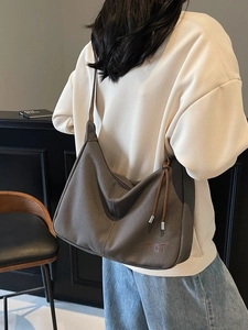 Graue Retro-Hobo-Schultertasche aus Canvas mit TGT-Logo und braunem Kordelzug am Model getragen