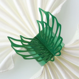 Close-up of laser-cut green leaf napkin ring on white silk fabric for party decor