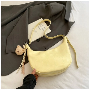 Detail of light yellow crescent shoulder bag with crocodile texture and bear charm