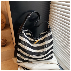 Detail of striped mesh tote bag featuring a leather strap and wooden horn button closure