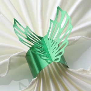 Close-up of green metallic hollow leaf napkin ring on white satin fabric for party decor