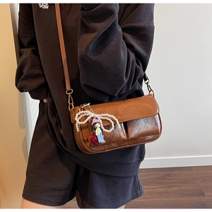 Detail of brown faux leather crossbody bag featuring vintage texture and pearl charm