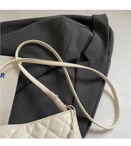 Gros plan d'un sac seau matelassé beige avec bandoulière en cuir nouée sur fond sombre