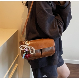 Detail of brown leather pillow bag with pearl bow and red heart charms on a shoulder strap