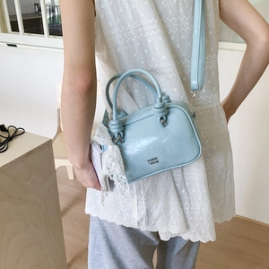 Hellblaue glänzende Handtasche mit weißem Spitzenbesatz und metallischem Markenlogo