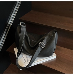 Detail of black pebbled leather crescent bag with silver buckle on a vintage book