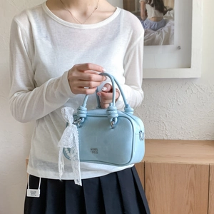 Detail einer hellblauen Handtasche aus Leder mit weißer Spitzenschleife und Perle