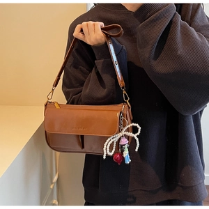 Detail of dark brown leather pillow bag with pearl bow and cartoon doll charms