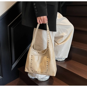 Sac hobo en similicuir beige avec clous argentés porté par un mannequin dans un cadre intérieur