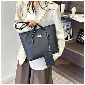 Detail of black pebbled leather tote bag with metal logo and matching small card pouch