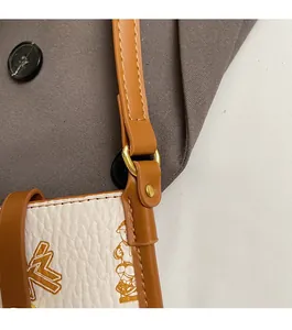 Detail of golden metal ring hardware and brown leather strap on a printed shoulder bag