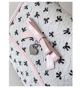 Detail einer geprägten Ledertasche mit rosa Schleife und silbernem Herzanhänger