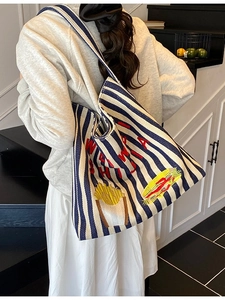 Grand sac cabas en toile rayé bleu et blanc avec broderie rouge porté par un mannequin