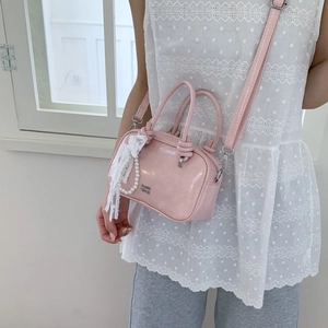 Detail einer rosa glänzenden Mini-Handtasche mit Perlen-Spitzen-Anhänger und Logo