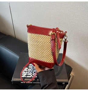 Close-up of beige woven straw shoulder bag with red faux leather trim on a book