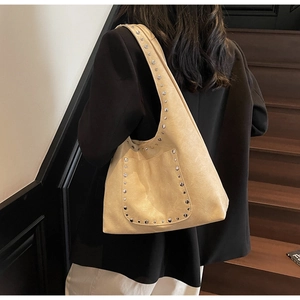 Sac hobo beige à rivets argentés porté par un mannequin pour un style urbain chic