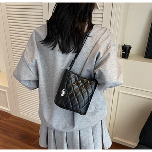 Détail du sac seau matelassé noir avec pendentif en argent porté par le mannequin