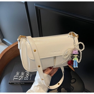 Detail of white leather shoulder bag featuring an embossed logo and a trendy charm pendant