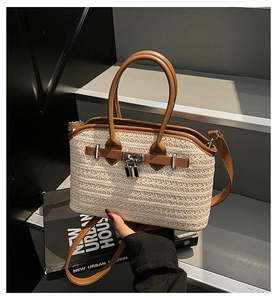 Close-up of cream woven straw handbag featuring brown leather accents and silver lock